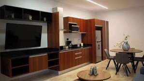 A modern kitchen with wooden cabinets, a black countertop, and a built-in oven. There is a dining area with a round table and chairs. - Urban Refuge, Loft with pool and cowork (Mérida)