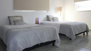 A room with two beds, beige curtains, a lamp, and a window.