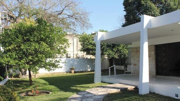 A modern building with a covered outdoor area, a stone pathway, and a well-maintained garden.
