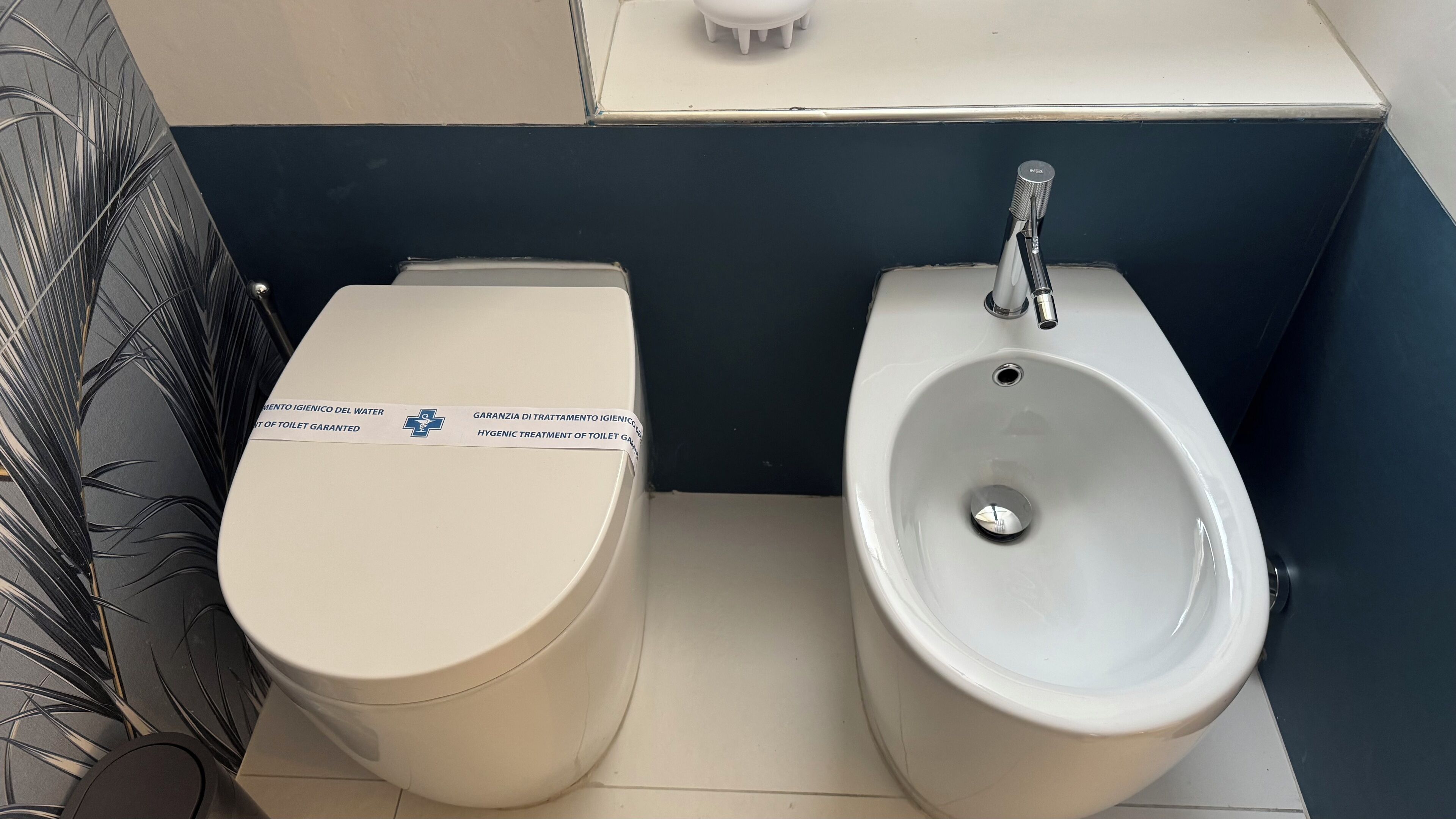 Een toilet en een bidet in een badkamer met een donkere wand en een witte vloer.