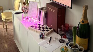 Un salon moderne doté d’un grand téléviseur diffusant une scène de plage, d’un jeu d’échecs, d’un mot de bienvenue, d’une bouteille de champagne et d’un vase décoratif.