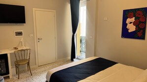 Une chambre d’hôtel avec un lit, un bureau et une chaise, une télévision, un tableau et une fenêtre avec des rideaux.