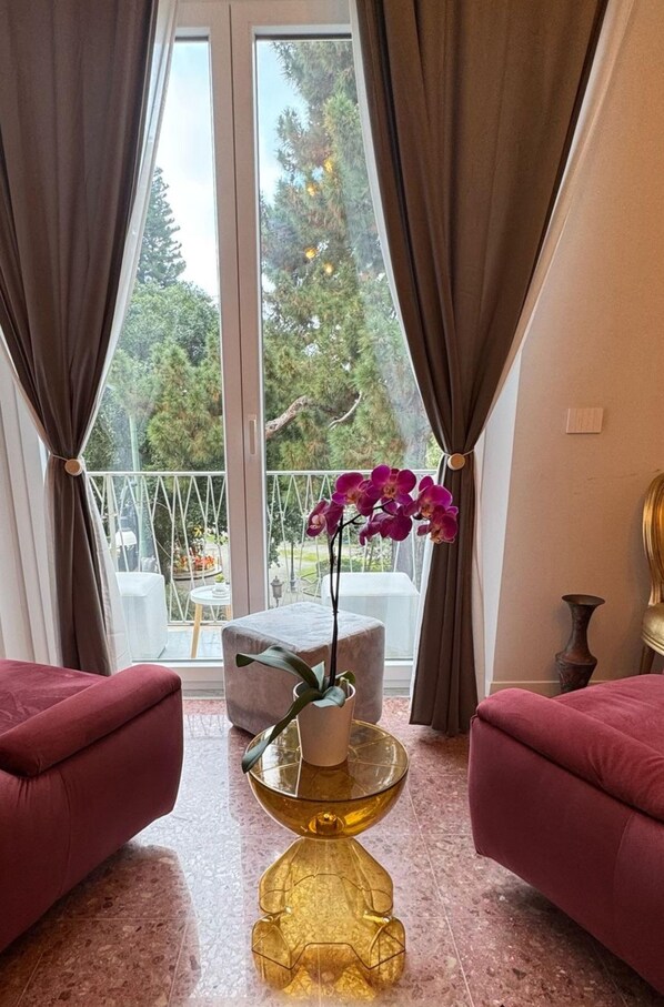 A room with two red sofas, a glass table with a gold base, and a window with curtains.