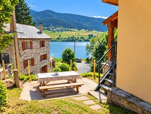 A stone building with a wooden table and benches, a staircase, and a view of a lake and mountains.