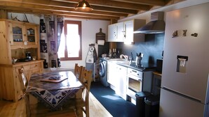 Een keuken met houten kastjes, een eettafel, een wasmachine en een koelkast.