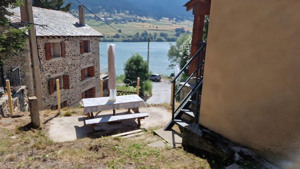 Een gebouw van steen met een houten trap, een picknicktafel en uitzicht op een meer en bergen.
