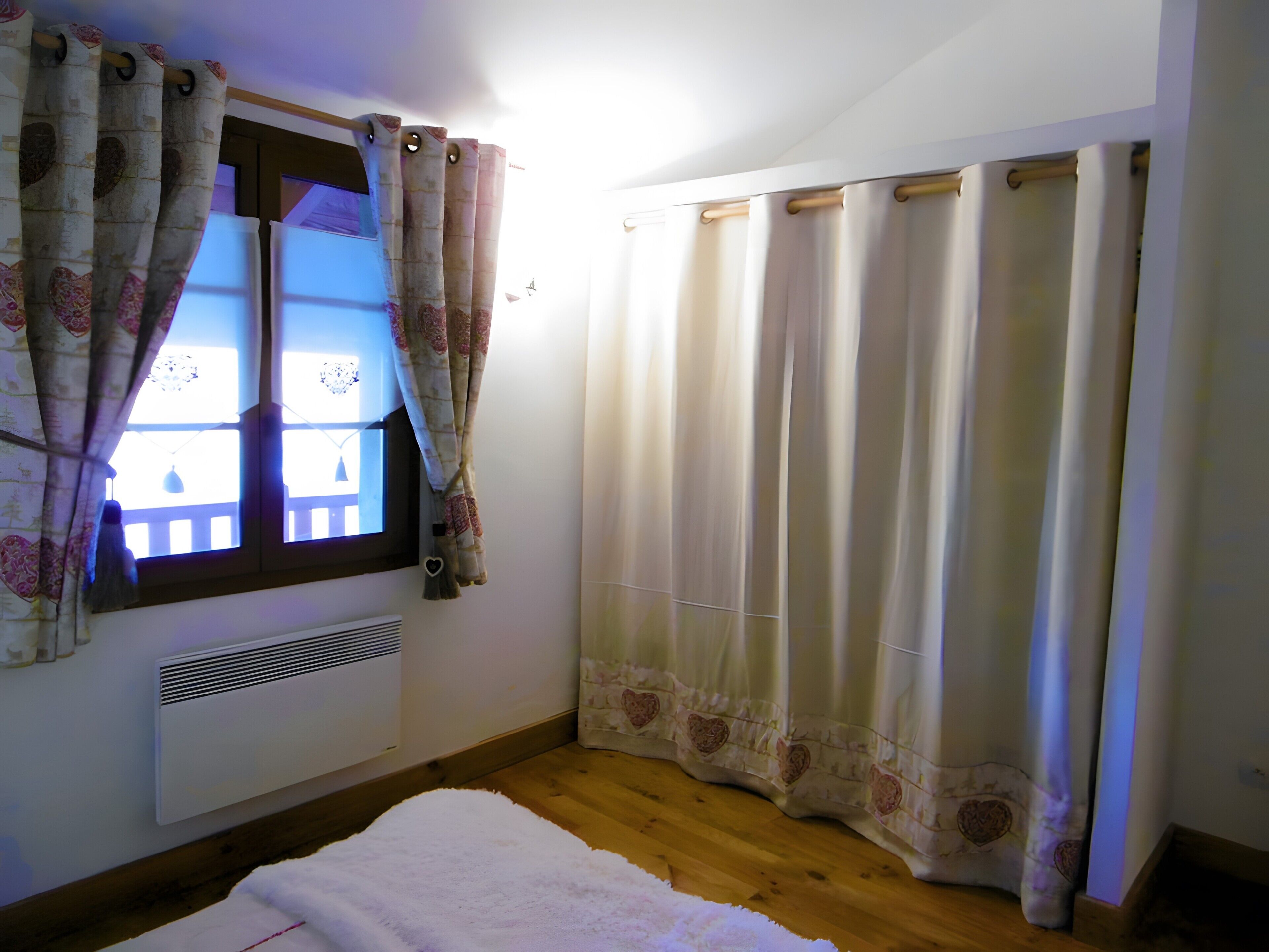 Een slaapkamer met een raam, gordijnen, een radiator en een wit tapijt.