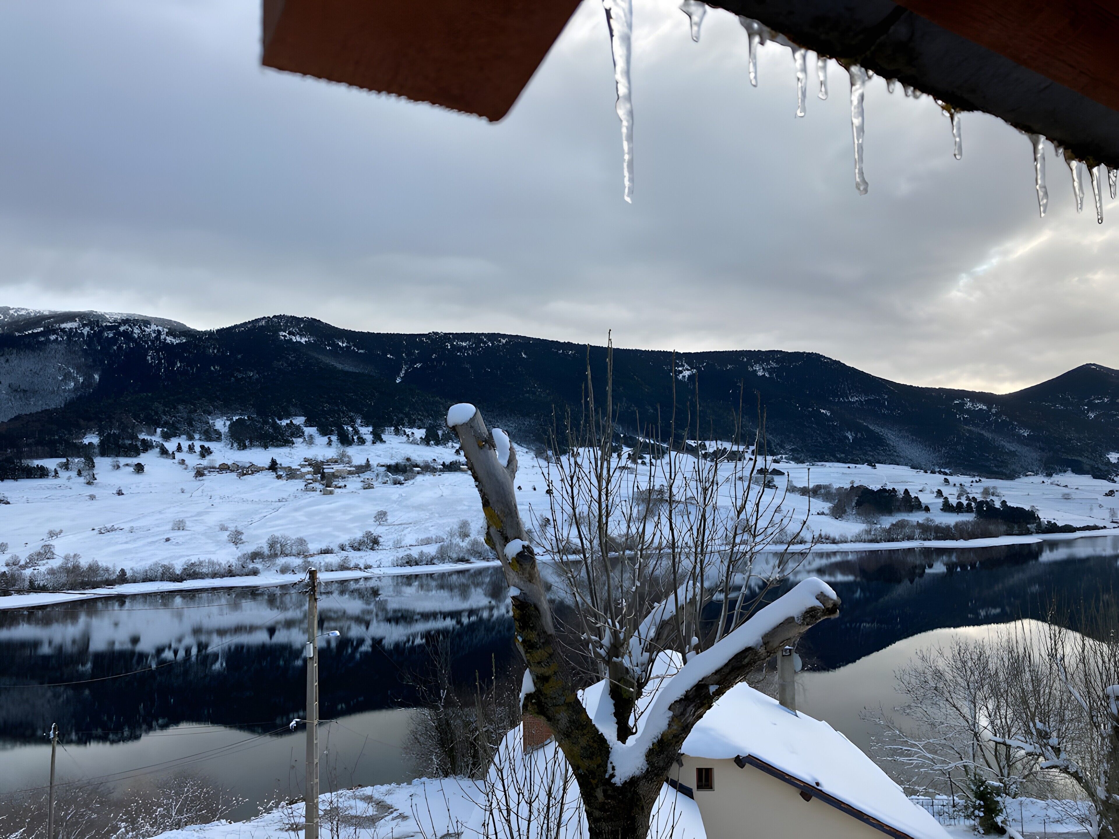 Paisagem nevada com um lago, montanhas e uma árvore coberta de neve.