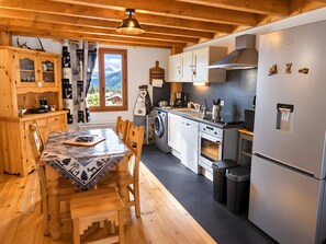 A kitchen with wooden cabinets, a dining table with chairs, a washing machine, and a refrigerator.