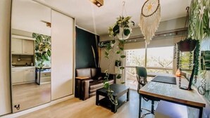 Un espacio moderno para la vida diaria con sofá, mesa de centro y comedor. Hay plantas y un atrapasueños colgando del techo.