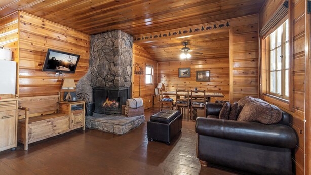 A cozy cabin interior with a stone fireplace, wooden walls, a leather sofa, and a dining area. - True Big Bear Lake Cabin with jacuzzi (Big Bear Lake)