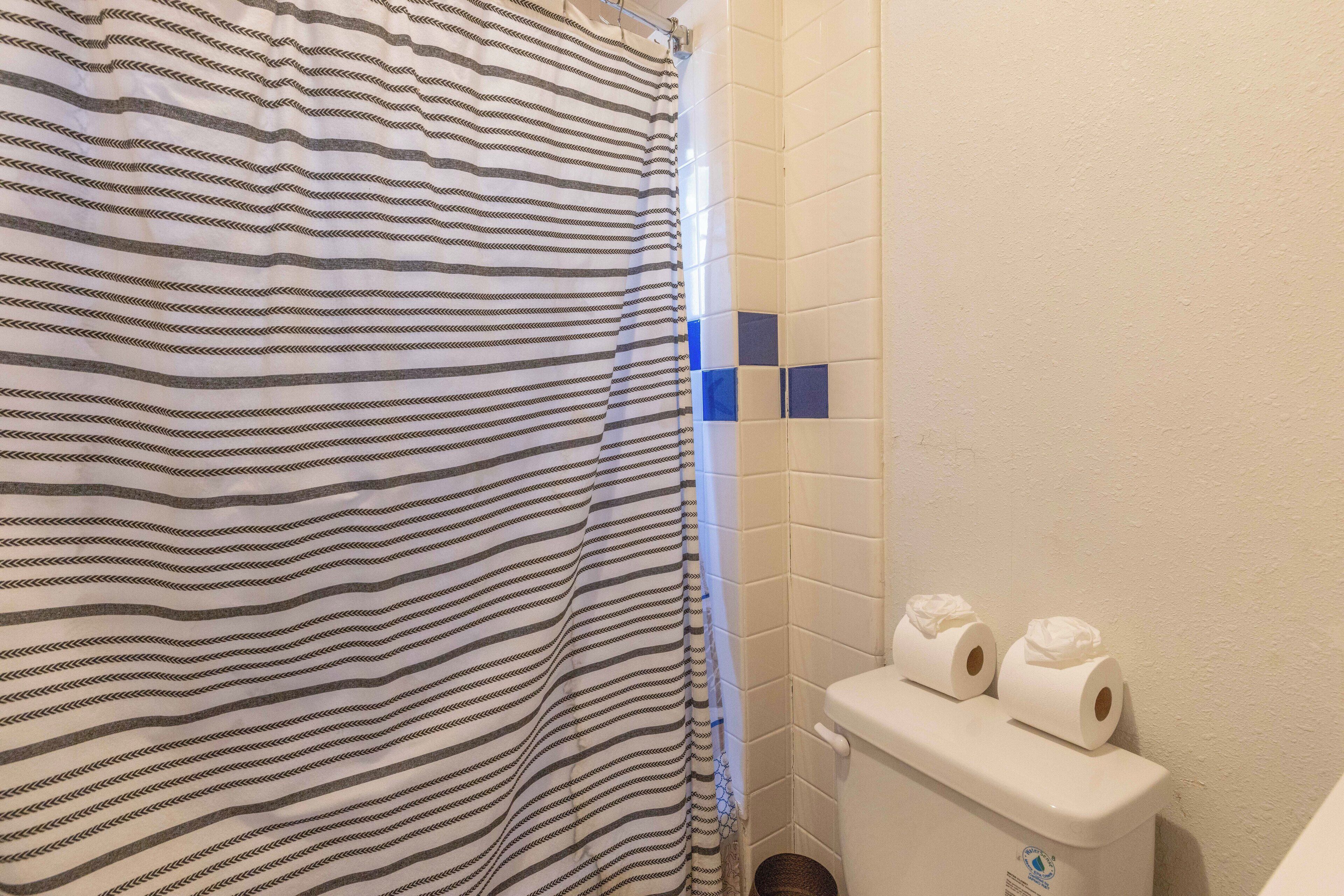 Un baño con cortina de ducha a rayas, un inodoro con dos rollos de papel higiénico y una pared con azulejos.
