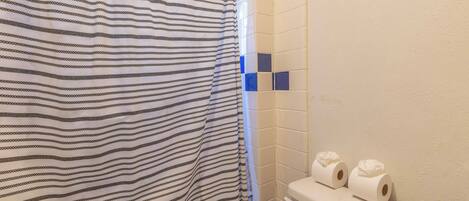 Un baño con cortina de ducha a rayas, un inodoro con dos rollos de papel higiénico y una pared con azulejos.