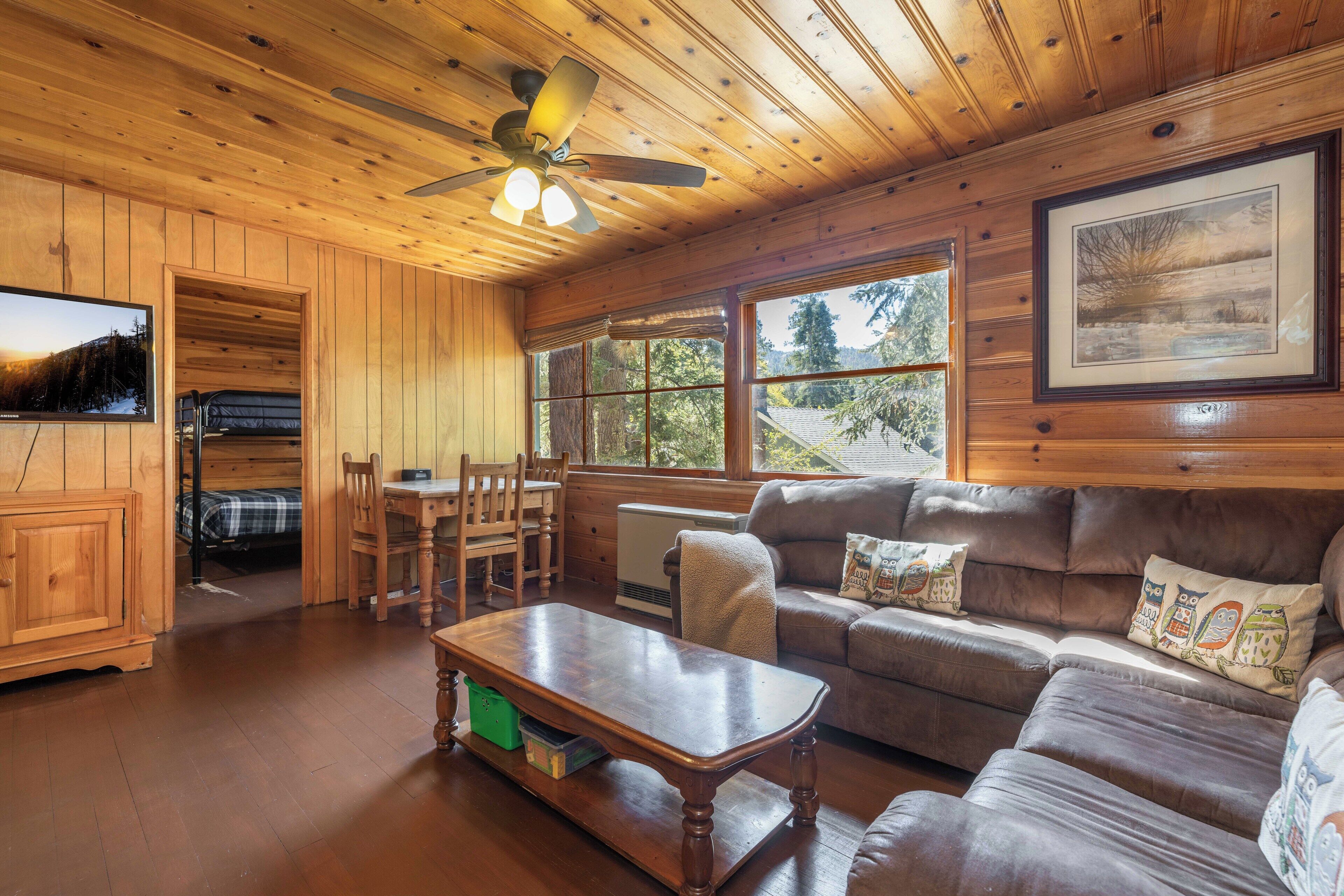 L’intérieur d’un chalet en bois comprend un coin repas, un canapé et un ventilateur de plafond.
