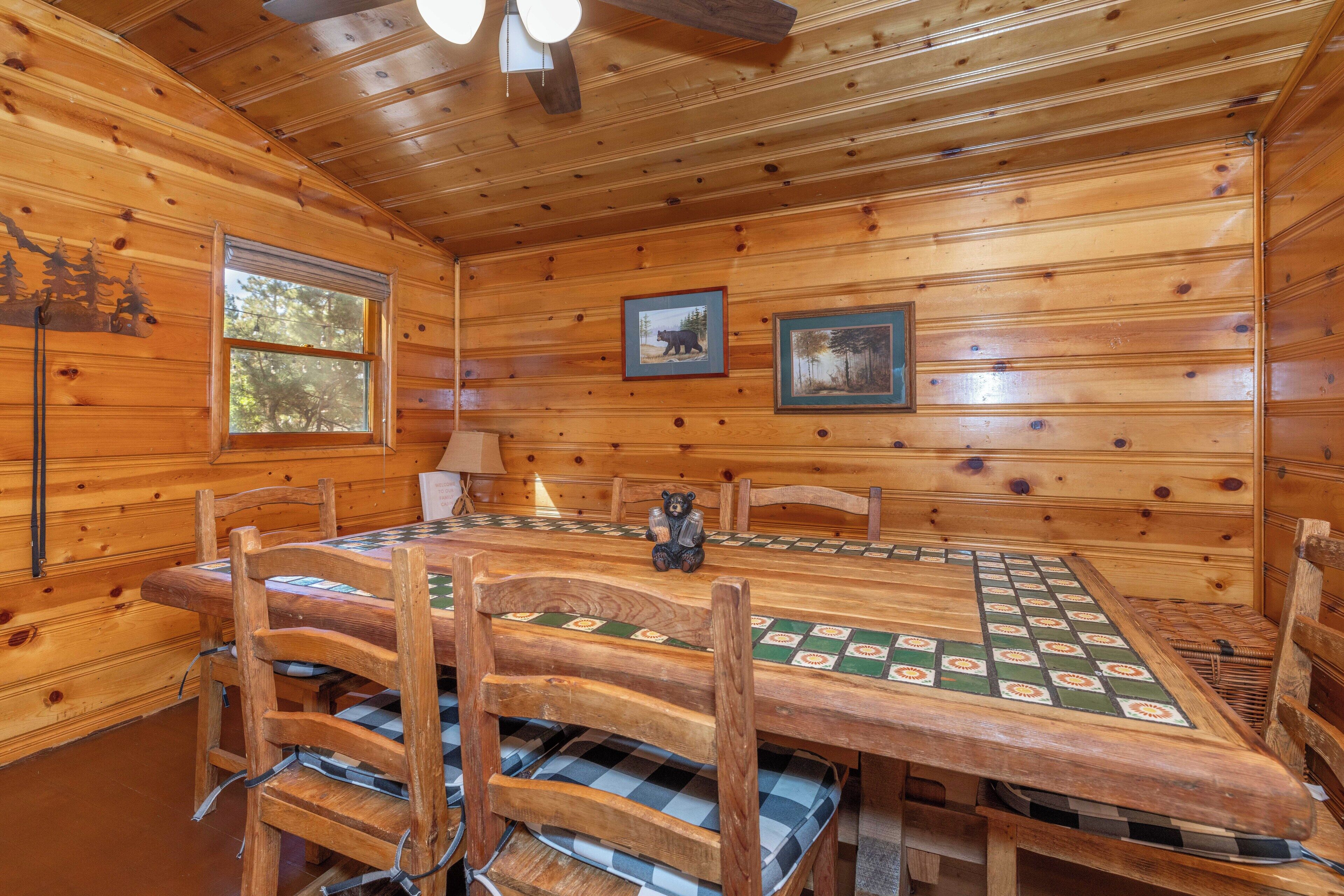 A wooden cabin interior with a large dining table, chairs, and two framed pictures on the walls.