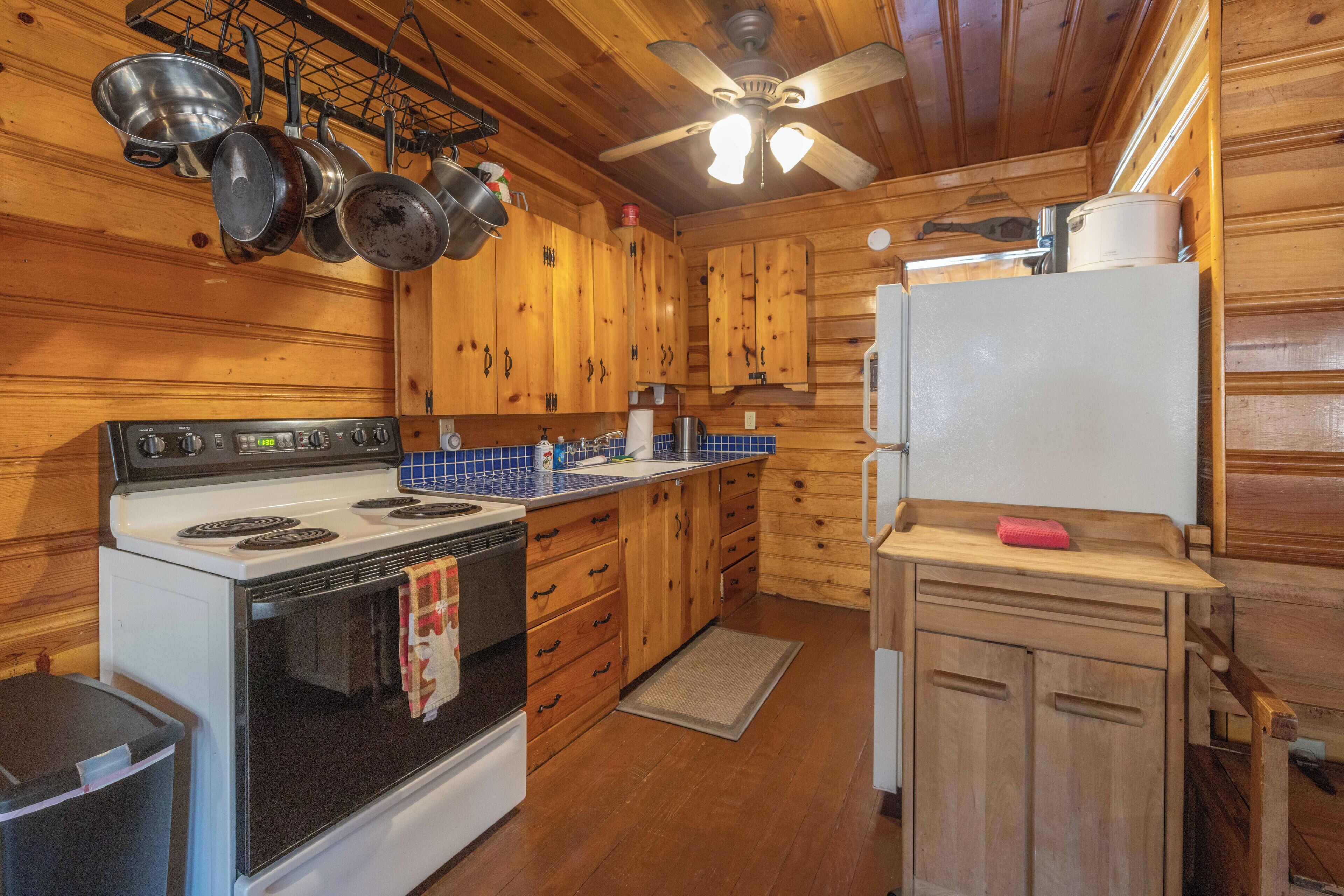 A wooden cabin kitchen with a stove, oven, and hanging pots.