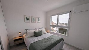 Un dormitorio con cama, mesitas de noche y ventana con vista a la ciudad.