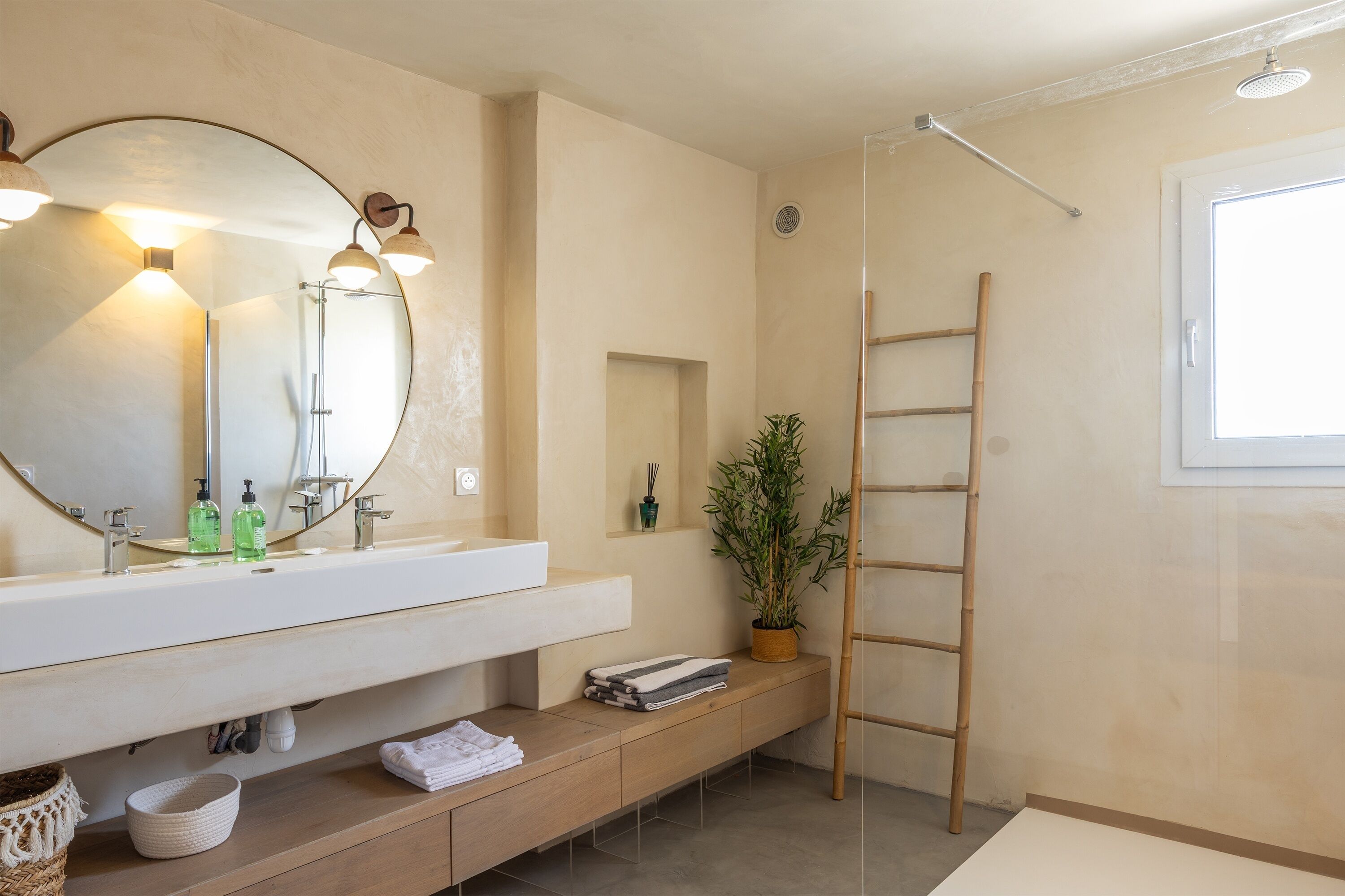 A modern bathroom with a large mirror, dual sinks, a shower, and a wooden ladder.