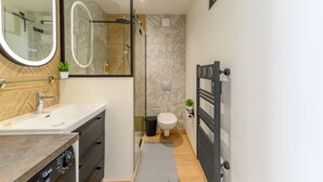 Ein modernes Badezimmer mit Duschkabine aus Glas, einem weißen Waschbecken und einem schwarzen Handtuchhalter.