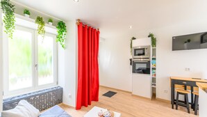 Ein modernes Wohnzimmer mit einer Couch, einem kleinen Tisch, einer Küchenzeile mit Geräten und einem an der Wand befestigten Fernseher.