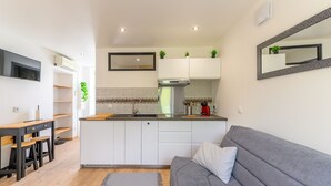 Eine moderne Küche mit weißen Schränken, einem grauen Sofa und einem an der Wand befestigten Flachbildfernseher.