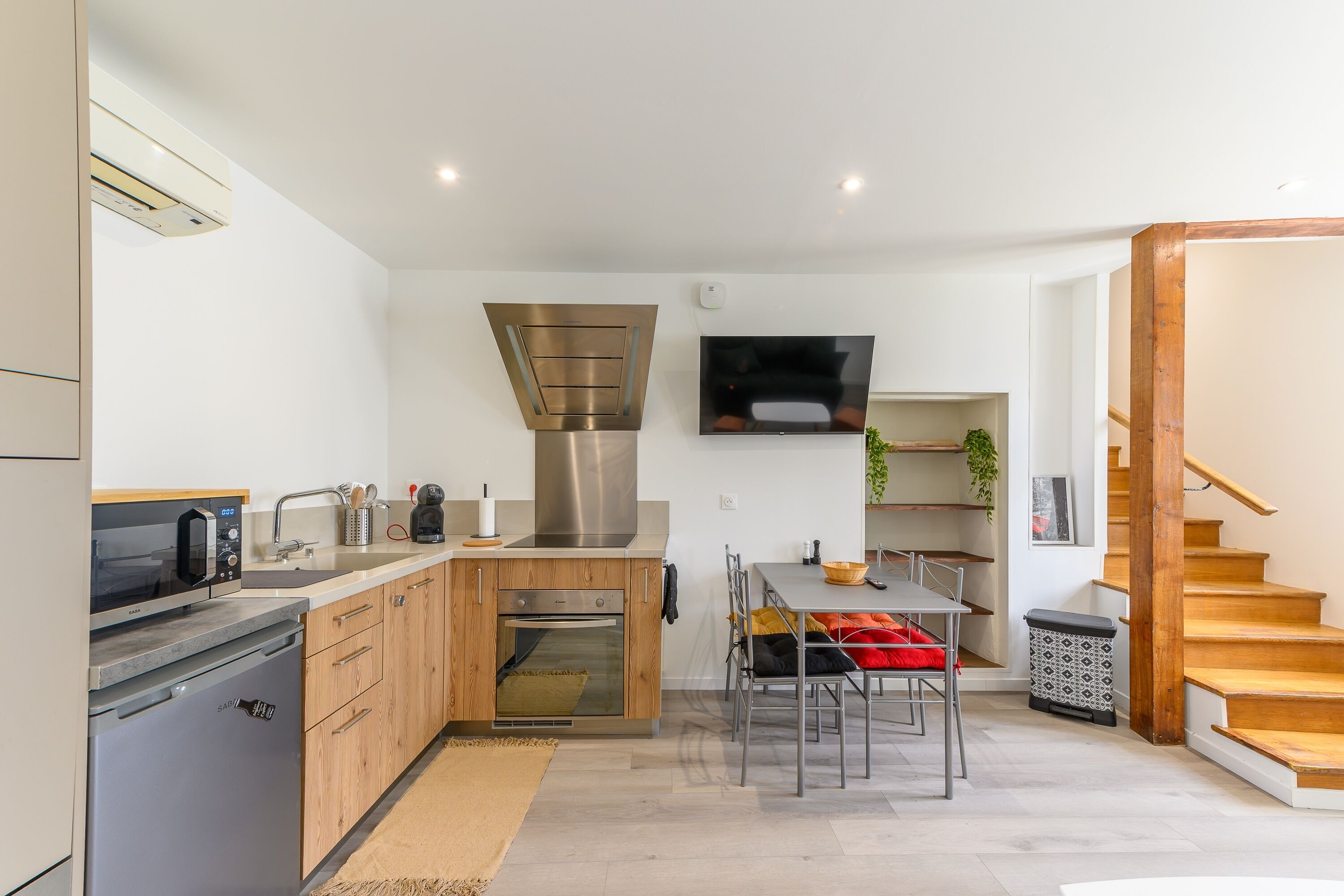 A modern kitchen with built-in appliances, a dining area with a wooden table and chairs, and a staircase leading to another level.