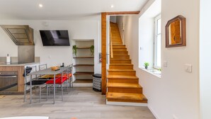 Ett modernt kök med en inbyggd ugn, en matplats med bord och stolar, en trätrappa och en tv som är monterad på väggen.
