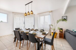 Een eetruimte met een tafel voor zes personen, stoelen, een hanglamp en een potplant.