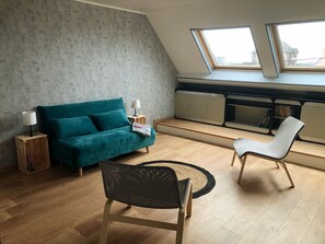 A modern living room with a teal sofa, a white chair, a small wooden side table, and a built-in bookshelf.