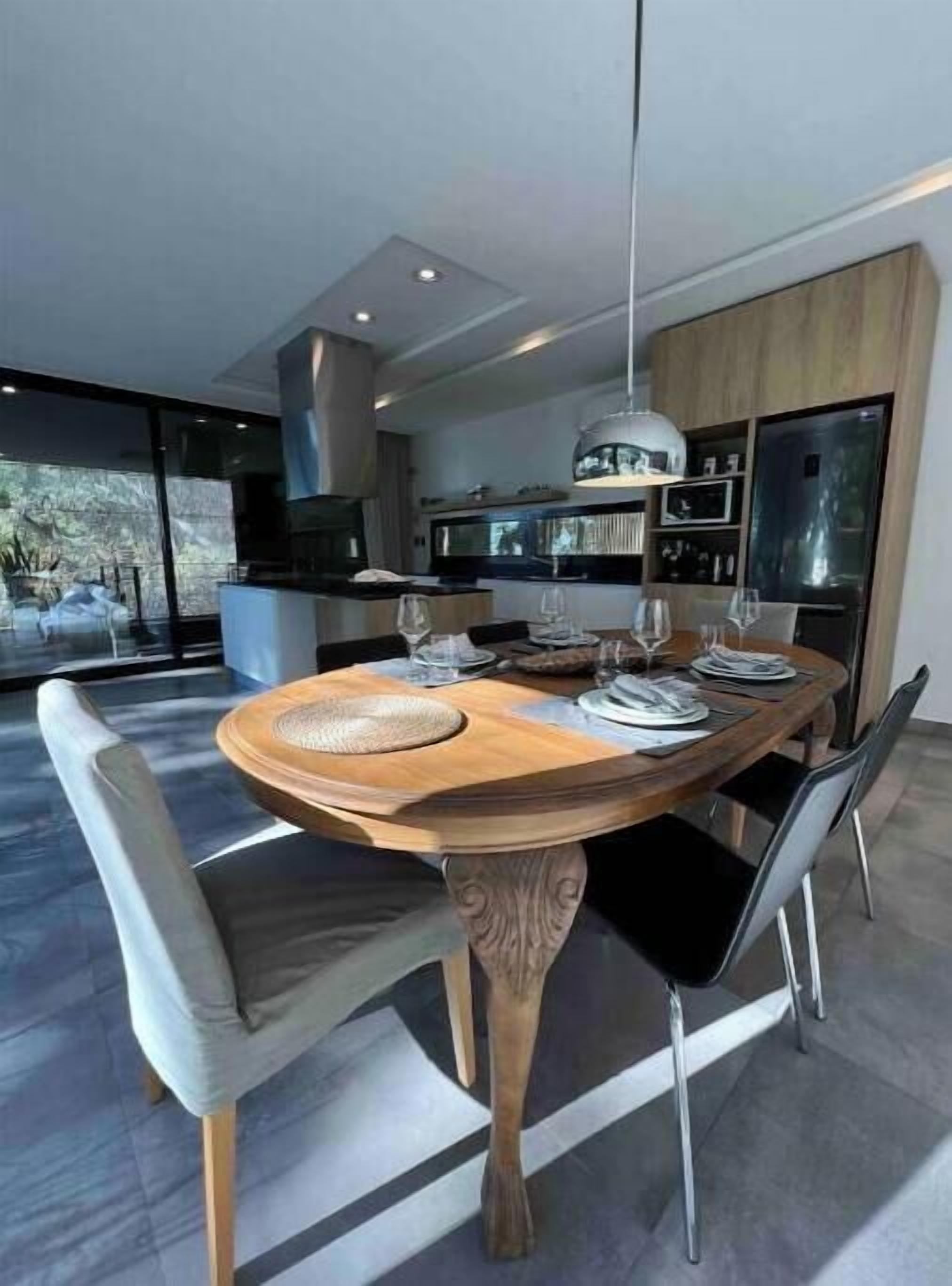 Uma sala de jantar moderna com mesa de madeira, quatro cadeiras e uma grande janela com vista para o exterior.