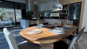 Uma sala de jantar moderna com mesa de madeira, quatro cadeiras e uma grande janela com vista para o exterior.