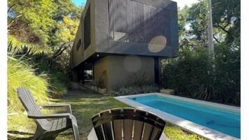 Uma casa moderna com piscina, duas cadeiras e um jardim.