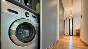 Une cuisine moderne équipée d’un lave-linge Samsung, d’un plancher en bois et d’un couloir menant à une porte.
