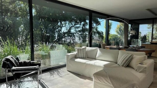 Un salon moderne avec une grande fenêtre, un canapé blanc et une chaise en métal.