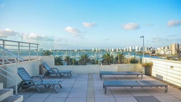 A rooftop terrace with lounge chairs and a view of a marina and city skyline. - Puerto Pileta Grill and Garage on the Peninsula (Punta del Este)