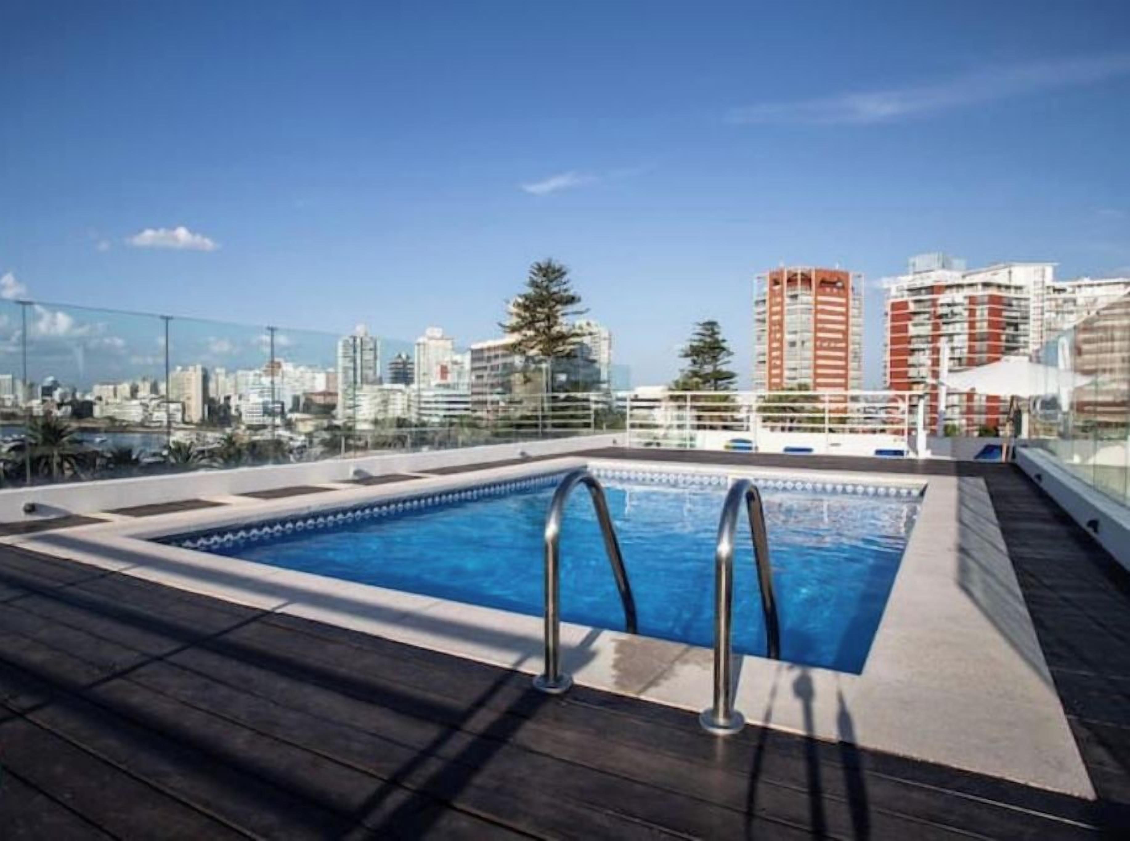 Una piscina sul tetto con vista sulla città, circondata da edifici e alberi.