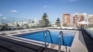 Una piscina sul tetto con vista sulla città, circondata da edifici e alberi.