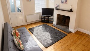 A living room with a sofa, a fireplace, a television, and a clock on the wall. - Entire Excellent Property on Mountcastle Road, Leicester (Leicester)