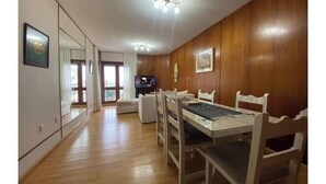 Een eethoek met een houten tafel en stoelen, een televisie en een grote spiegel aan de muur.