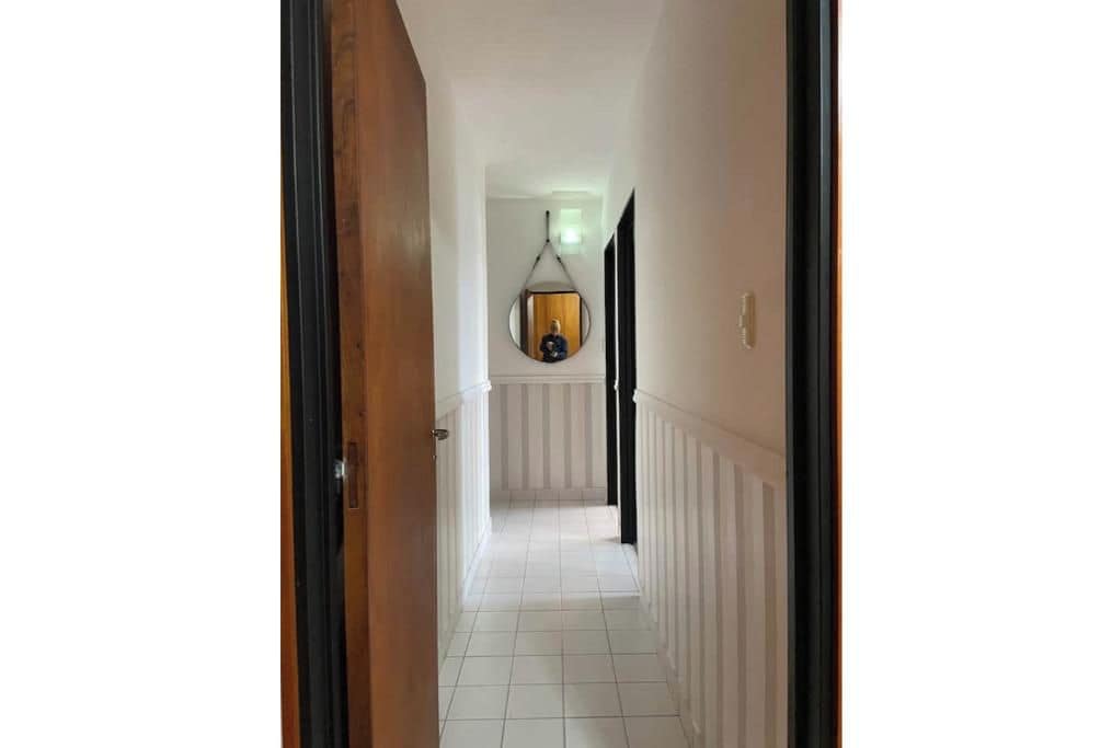 Un couloir doté d’un sol carrelé de carreaux blancs, d’un chambranle de porte en bois et d’un grand miroir rond suspendu au mur.