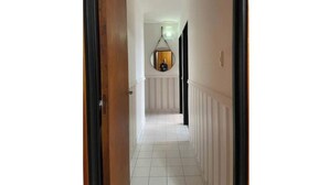 Een hal met witte betegelde vloer, een houten deurkozijn en een rond spiegel aan de muur.