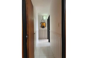 Un couloir doté d’un sol carrelé de carreaux blancs, d’un chambranle de porte en bois et d’un grand miroir rond suspendu au mur.