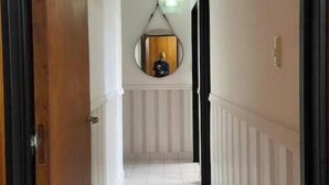 Een hal met witte betegelde vloer, een houten deurkozijn en een rond spiegel aan de muur.