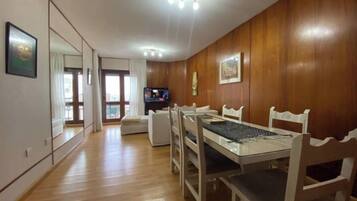Un comedor con una mesa y sillas de madera, un televisor y un espejo grande en la pared.