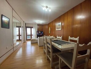 Un coin repas avec une table et des chaises en bois, un téléviseur et un grand miroir au mur.