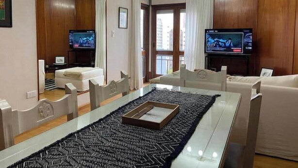 Een moderne woonkamer met een glazen eettafel, twee banken, een televisie en een grote spiegel.