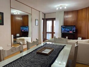 A modern living room with a glass dining table, two sofas, a TV, and a large mirror. - Beautiful 10th Floor Quality Full Park Zone (Paraná)