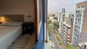 Een hotelkamer met een bed, een tafeltje en uitzicht op een stadsbeeld door een raam.
