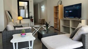 Un salon moderne avec un canapé, une petite table sur laquelle est posée une plante, un téléviseur sur un meuble et une bibliothèque.