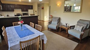 Amplia sala de estar con mesa de comedor, dos sillones, un sofá y una cocina al fondo.